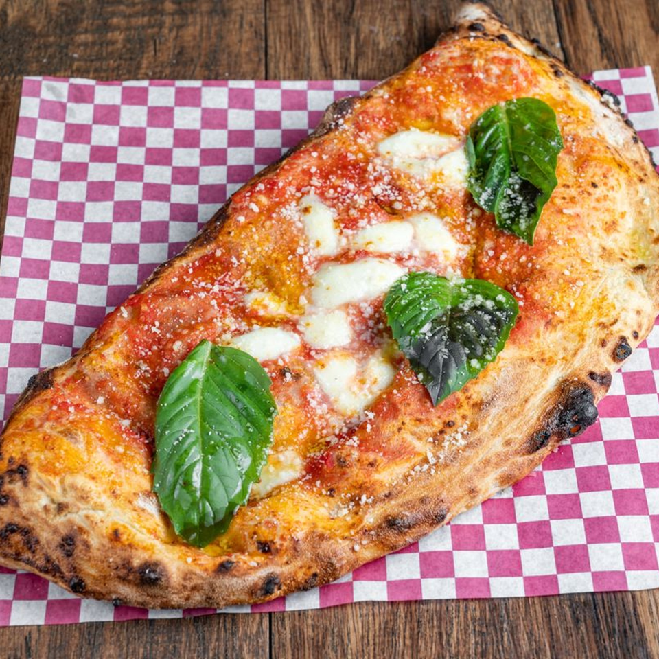 Blue Boy Pizza's calzone with tomato sauce, melted cheese, and fresh basil on checkered paper.