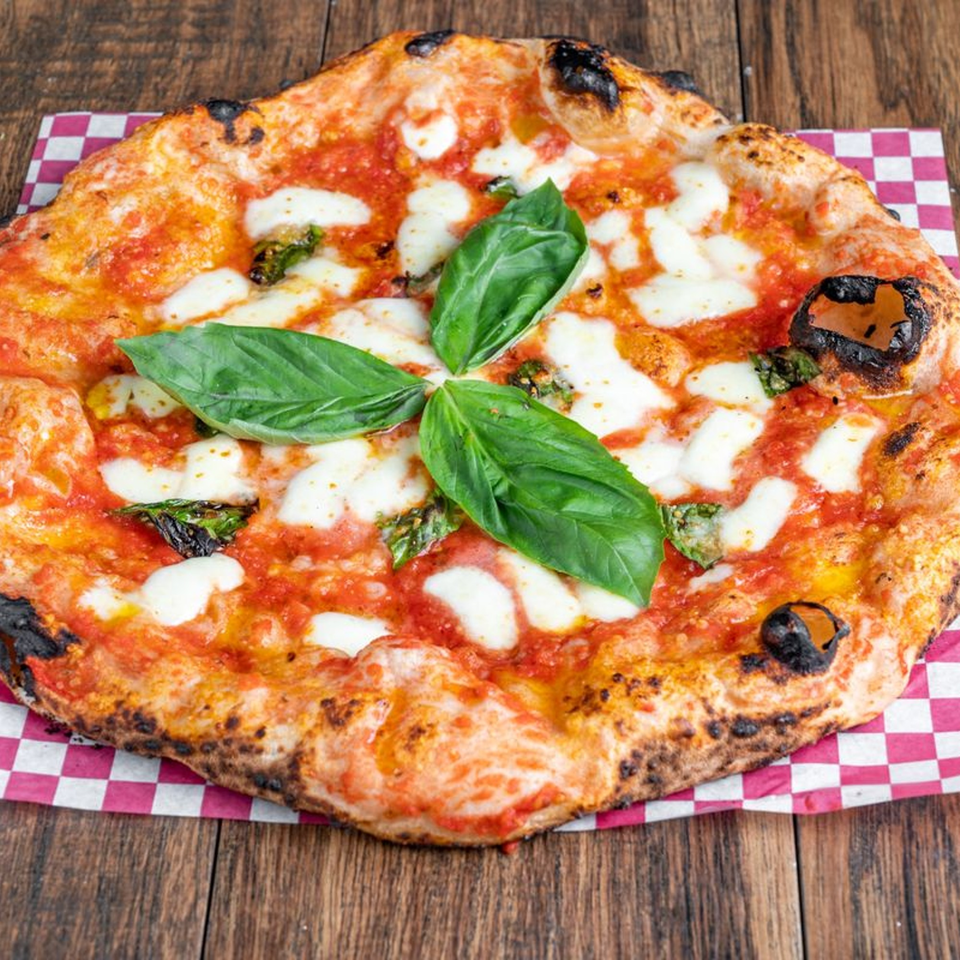 Blue Boy Pizza's Margherita pizza with fresh basil leaves, mozzarella, and tomato sauce on a checkered paper.